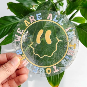 Detail of round suncatcher sticker featuring a smiley face and motivational text