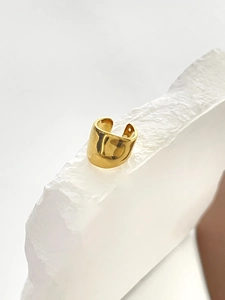 Detailed view of gold horseshoe-shaped ear cuff on white textured stone background