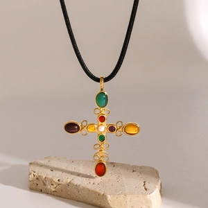 Dettaglio di un ciondolo a croce in oro 18k con pietre colorate su cordino nero intrecciato