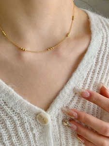 Close-up of minimalist gold beaded necklace worn over a white textured knit sweater