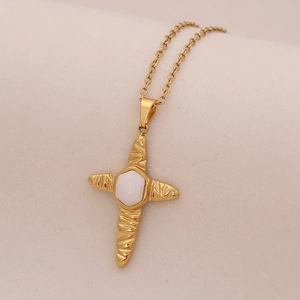 Macro detail of a gold cross pendant with white hexagon stone inlay and textured arms