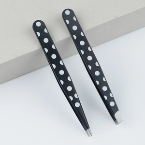 Black polka dot eyebrow tweezers set with slanted and pointed tips on minimalist background