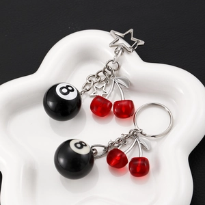 Red cherry and black billiard 8-ball keychains with star charms on a white ceramic tray