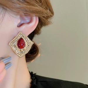 Macro detail of retro gold rhombus earring with red gemstone on model's ear