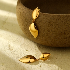 Polished 18K gold double leaf teardrop earrings shown on a rustic ceramic bowl