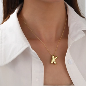 Close-up of golden letter K pendant necklace on model wearing a white shirt