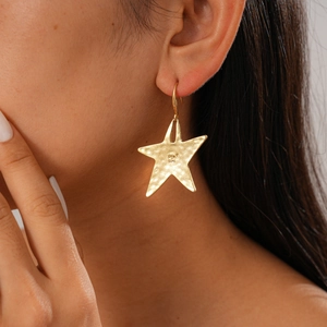 Macro shot of gold starfish earrings with hammered texture worn by a model