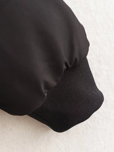 Détail de la veste de baseball noire montrant les poignets côtelés et le tissu
