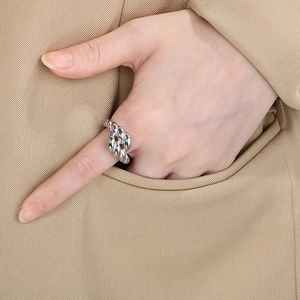 Close-up of a silver twisted rope ring design worn on finger against a beige suit fabric
