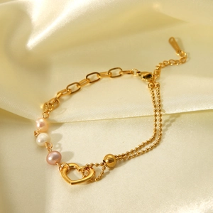 Detail of layered gold stainless steel bracelet with pearls and a hollow heart charm