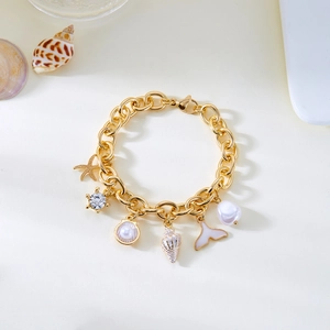 Gold ocean charm bracelet with starfish, pearls and shells on a white sandy background
