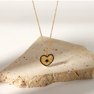 Detail of 18K gold heart pendant necklace featuring eye engraving and black crystals