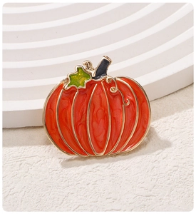 Detail of a pumpkin brooch with orange enamel and gold metal trim on a textured surface
