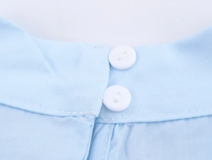Close-up of light blue shirt collar detail featuring white buttons and woven cotton texture