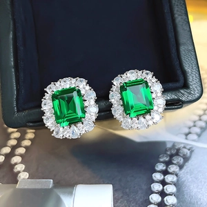 Macro shot of silver stud earrings featuring emerald cut green gems and crystal halos