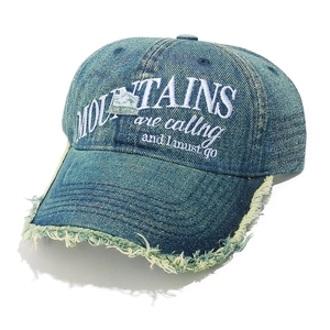 Detail of washed denim baseball cap with mountain embroidery and distressed brim edges