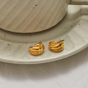 Elegant gold twisted C-shaped hoop earrings on a minimalist beige ceramic saucer