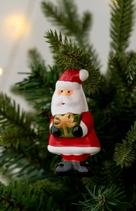 Close-up of Santa Claus ceramic ornament with gift box hanging on a Christmas tree