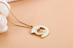 Detail of gold necklace with shell inlay and crystal C pendant on beige background
