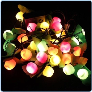 Colorful LED berry light string with green leaves and battery box on dark background