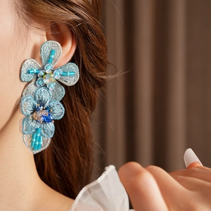 Detailed view of handmade blue embroidered flower earrings with intricate beadwork details