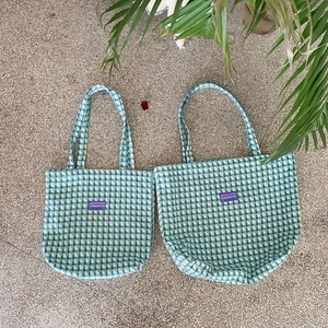 Flat lay of blue and white checkered woven tote bags in two sizes on a stone tile floor