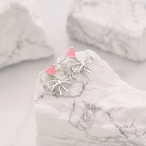 Detail of pink heart crystal and silver bow stud earrings on white marble surface