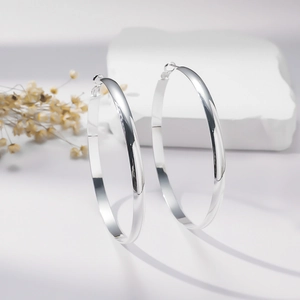 Minimalist large polished silver hoop earrings on decorative white stone background