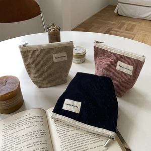 Three corduroy cosmetic pouches in cream pink and navy on a minimalist white table