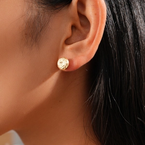 Close-up of golden woven knot stud earrings worn by a model showcasing texture