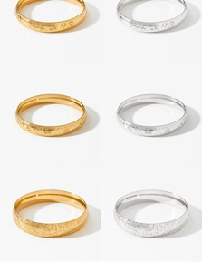 Detail view of gold and silver stainless steel bangles with intricate floral patterns