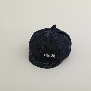 Detailed close-up of blue denim baby newsboy cap with white Hello embroidery and stitching