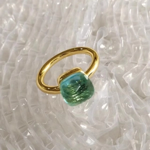 Close-up of golden ring featuring a square light teal zircon stone on bubble background