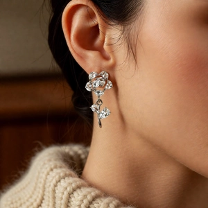 Close-up of a silver zircon flower drop earring on a model in a cozy white sweater