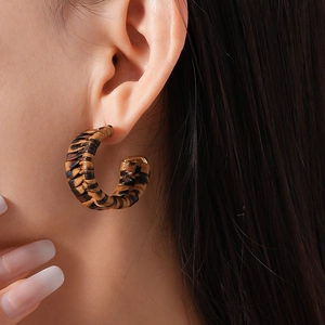 Macro side view of C-shaped leopard print faux leather woven earrings on a model