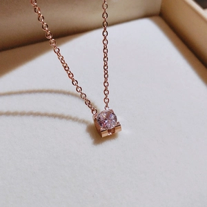 Macro shot of rose gold necklace featuring a single round zircon on beige velvet tray
