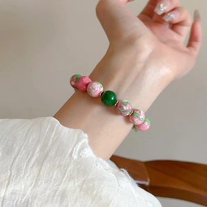 Detail of red and green gradient glass bead bracelet worn on wrist with gold spacers