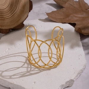 Close-up of chunky hollow line gold bangle on white textured stone with natural wood decor