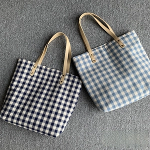 Detailansicht blau karierter Canvas-Totes mit verstärkten Kunstledergriffen und Nieten