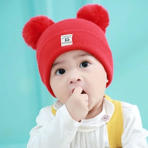 Close-up of red baby knit hat with double pom-poms and Moonlight label detail