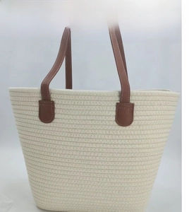 Detail of cream cotton woven tote bag featuring brown faux leather straps and white stitching