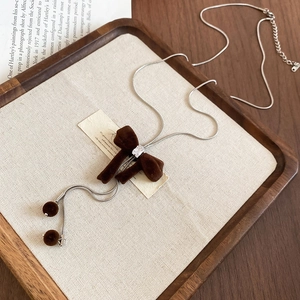 Detailed close-up of brown flocked bow pendant necklace with square zircon on silver snake chain