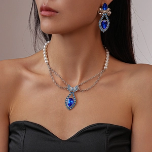 Detail of luxury necklace and earrings set featuring blue drop crystals and bow motifs