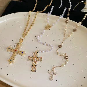 Vintage cross pearl necklaces with colorful gemstones and gold chains on a ceramic tray