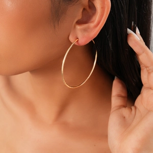 Close-up of a large golden geometric hoop earring worn by a model in soft lighting