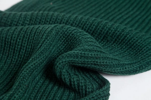 Close-up of green knitted fabric texture showing intricate stitch patterns and wool yarn
