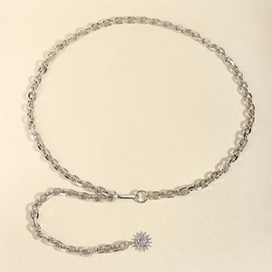 Detailed macro of silver metal chain belt with sunburst pendant on beige surface