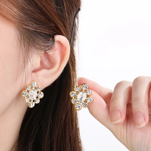 Close-up of gold stainless steel stud earrings with hollow flower pattern and white crystals