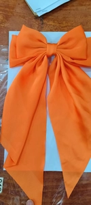 Detailed view of an oversized orange satin hair bow clip with elegant long ribbons