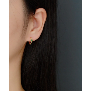 Close-up of a gold beaded hoop earring with a green emerald stone worn by a model